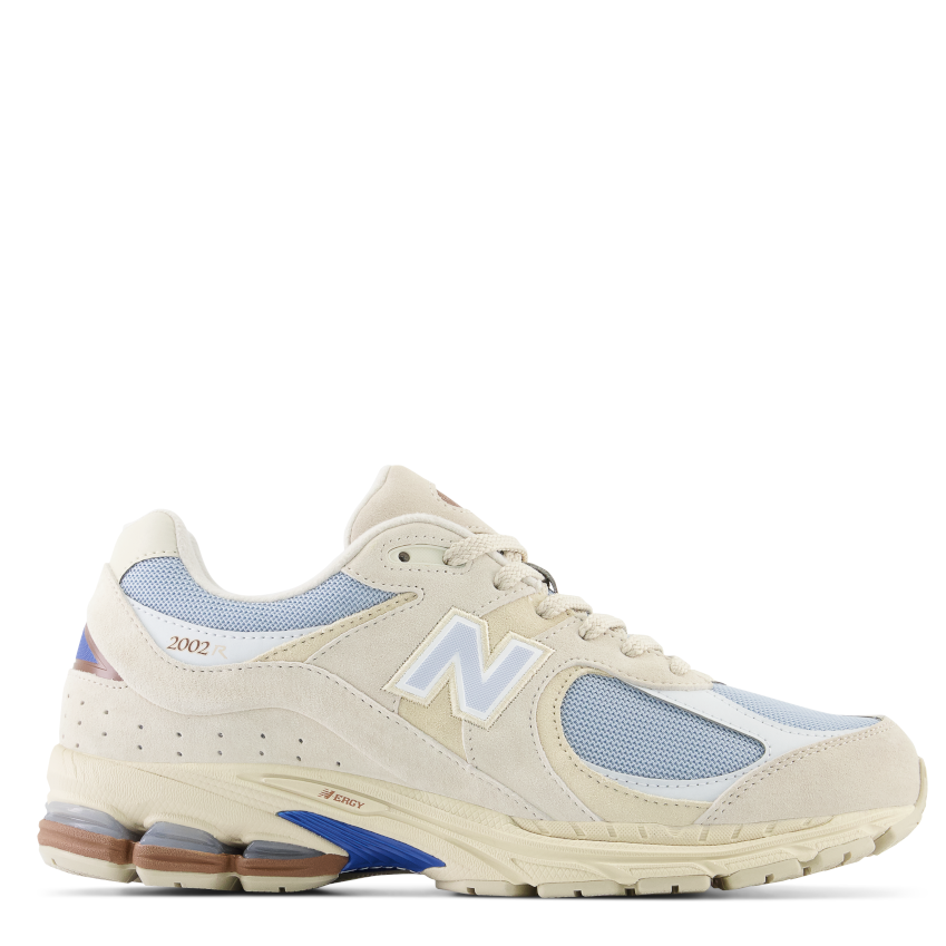 A pair of beige New Balance 2002R women's sneakers with blue accents and a mesh upper.