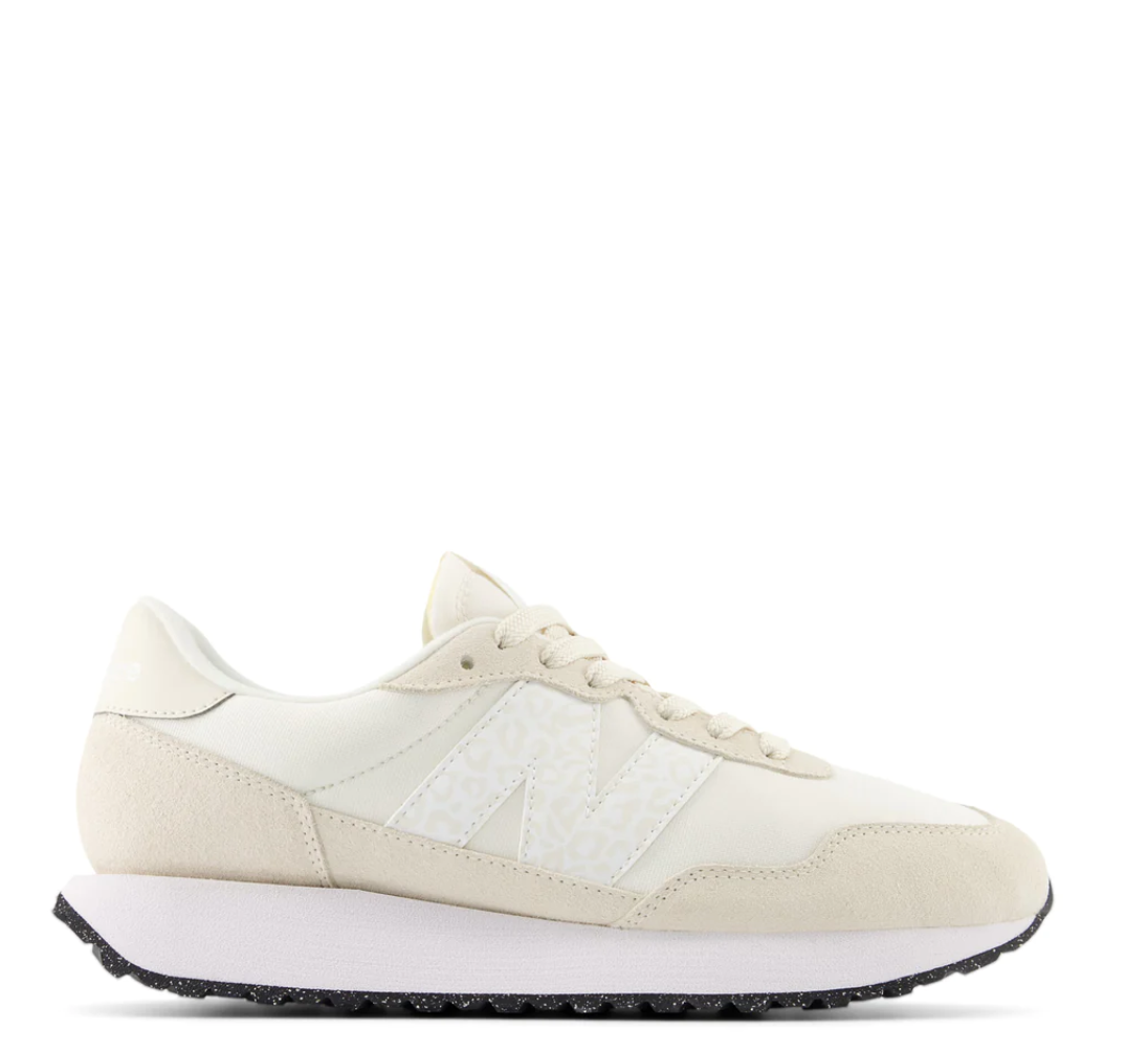 A pair of beige New Balance running shoes with lace-up closure, featuring a herringbone outsole and a midsole visible in the image.