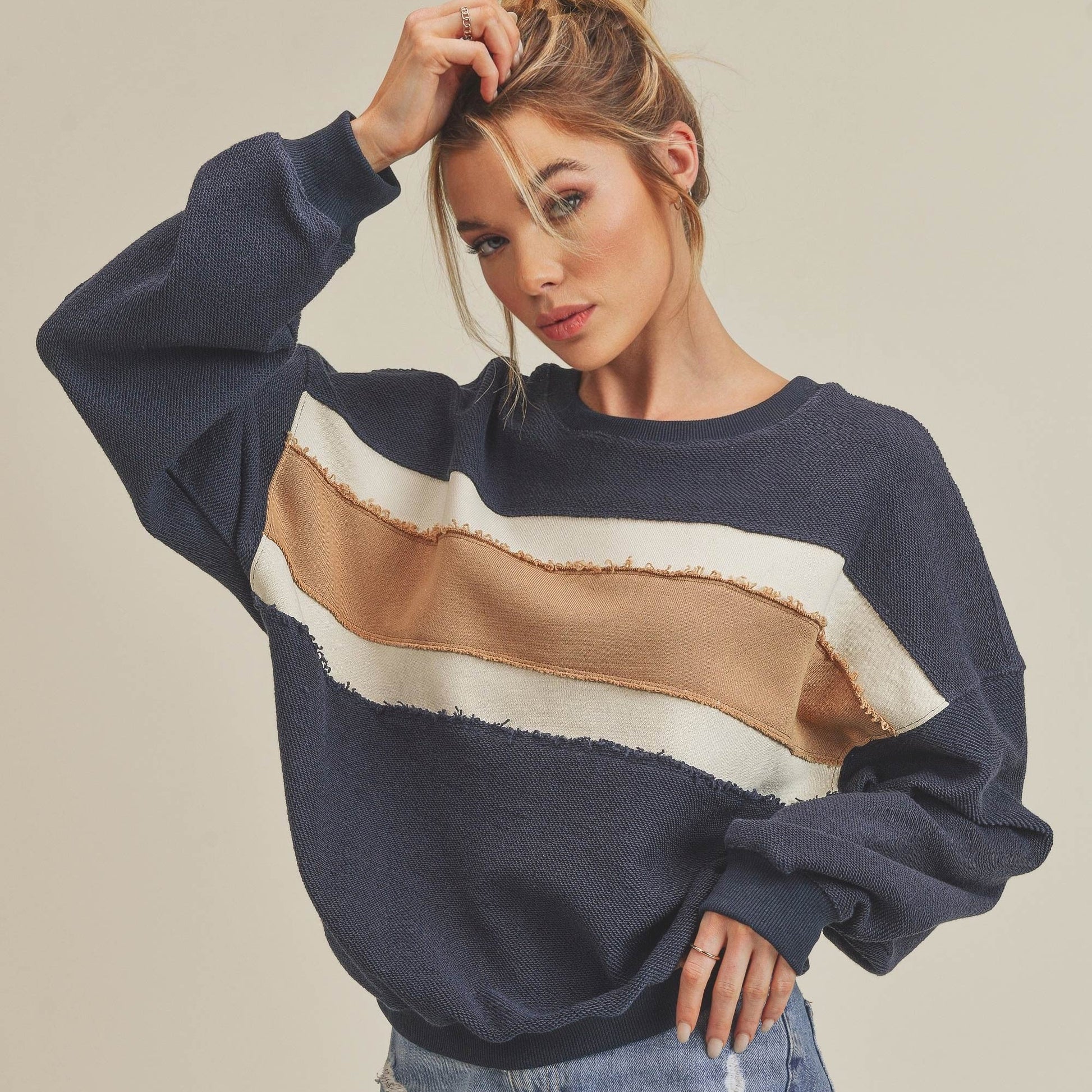 Woman wearing a navy sweater with color-block design and denim shorts on a beige background