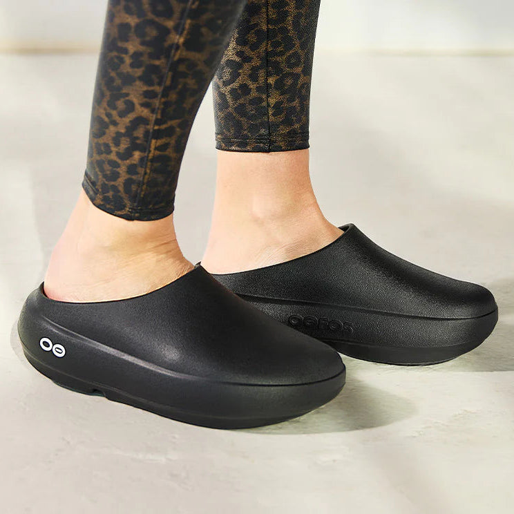 Person wearing black slip-on shoes with leopard print leggings on a light background