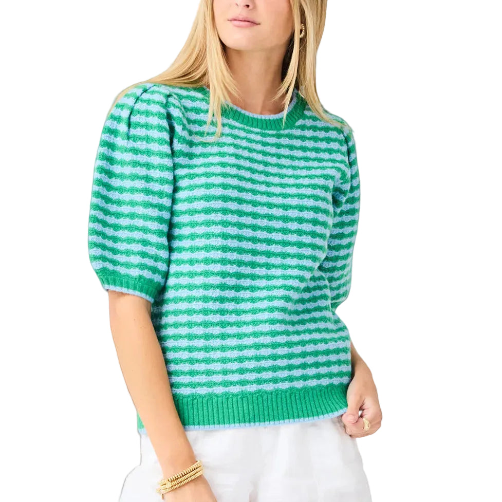 Woman wearing a green and white striped sweater with white shorts on a light gray background