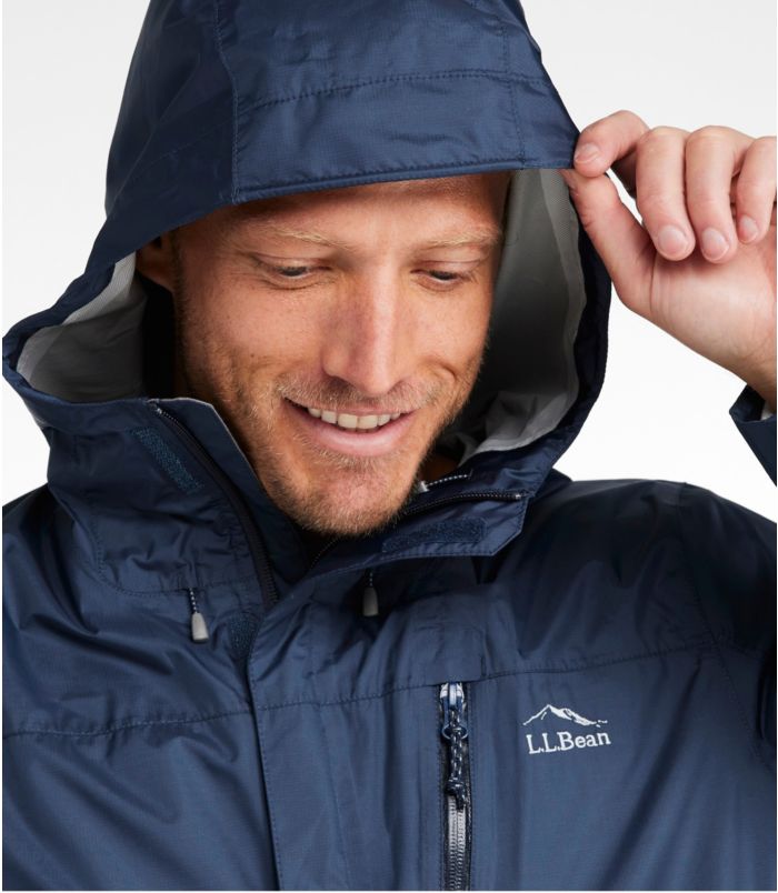 Man wearing a navy blue raincoat with a visible LL Bean logo, adjusting the hood against a white background.