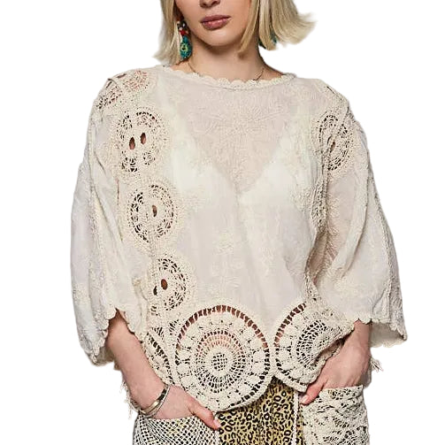 Woman wearing a bohemian outfit with a white top and patterned pants on a gray background