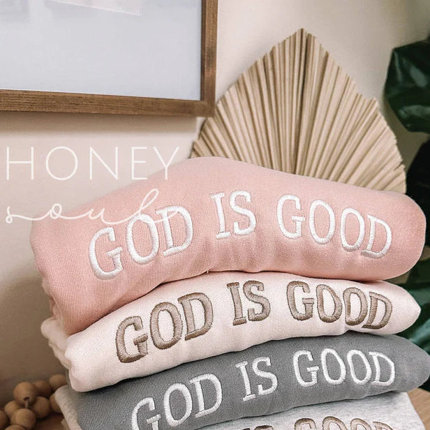 Stack of towels with 'GOD IS GOOD' text on a wooden surface, surrounded by decorative items.