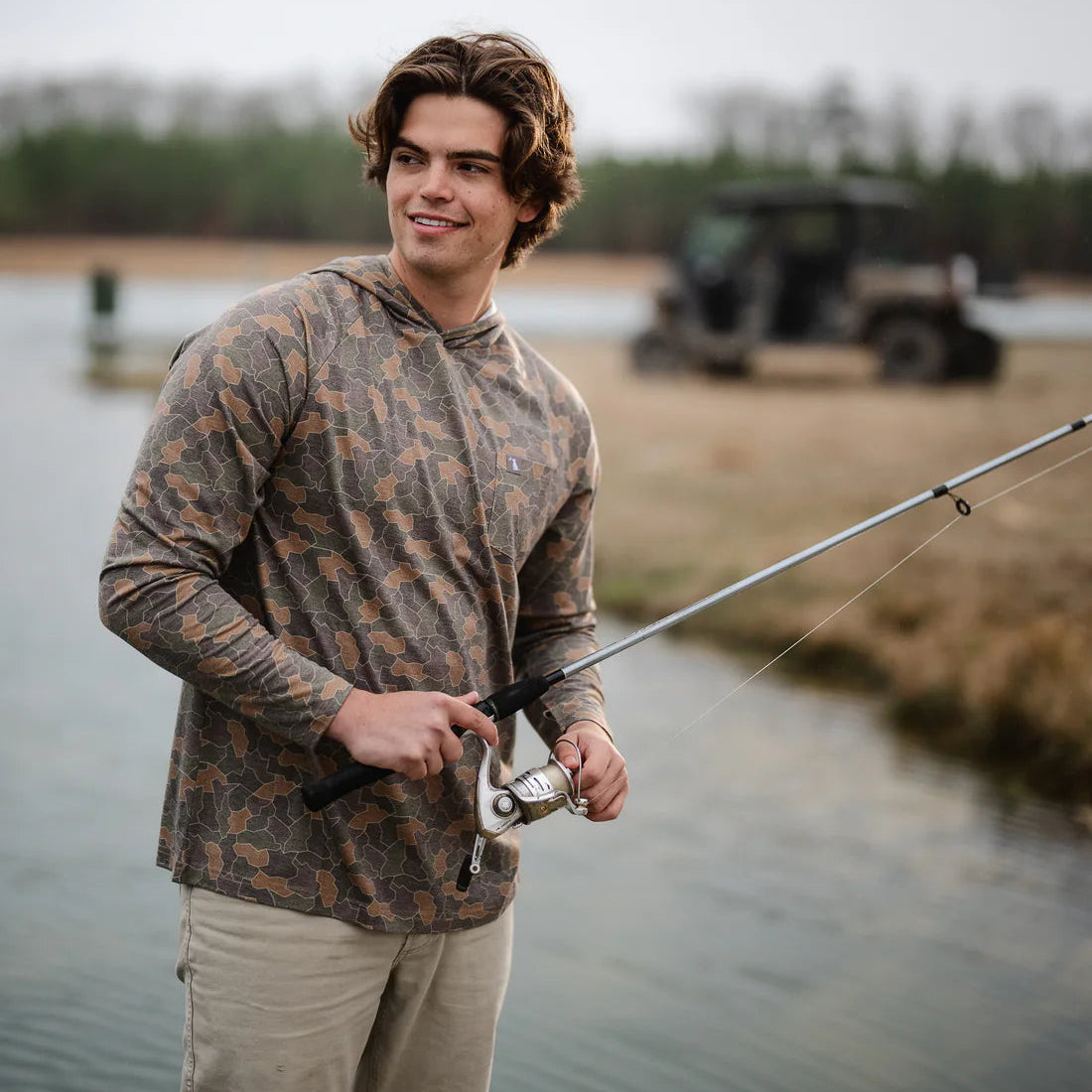 Man fishing by a lake with a vehicle in the background