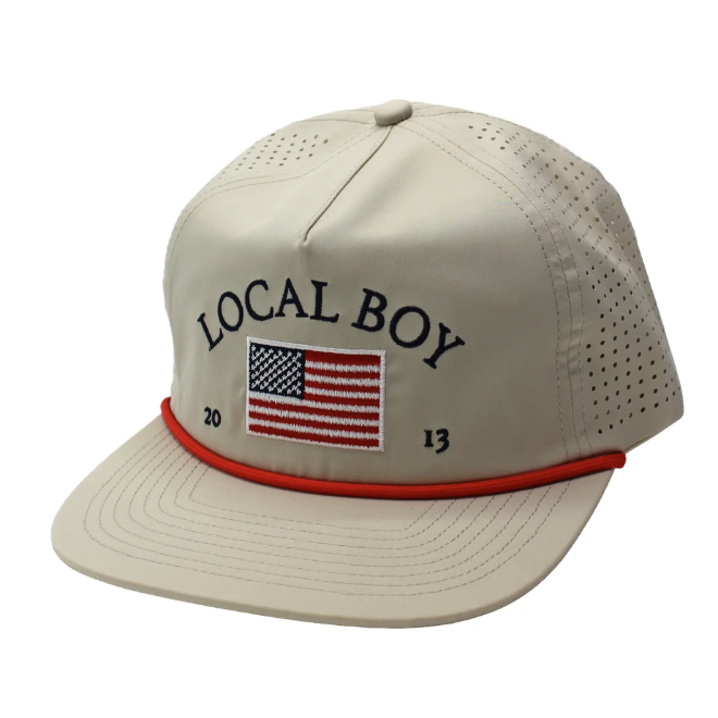 A beige baseball cap with 'LOCAL BOY' embroidered in navy on the front, an American flag patch, and a red brim stripe, shown on a white background.