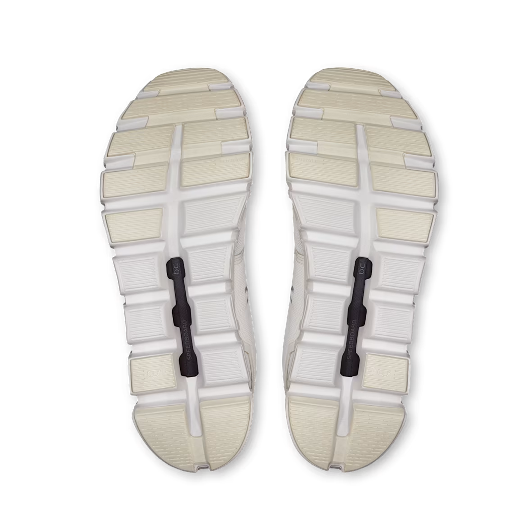 Top-down view of a pair of athletic shoes showing the textured white and beige outsoles with black hook-and-loop strap closures, set against a plain white background.