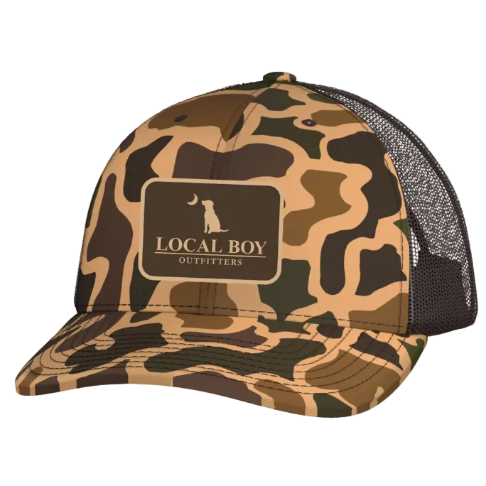 A camouflage trucker hat with a brown mesh back and a front patch reading 'LOCAL BOY OUTFITTERS' with a dog silhouette. A yellow 'NEW' badge appears in the top-left corner.