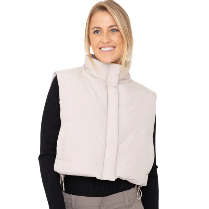 Woman wearing a beige vest over a black long-sleeve shirt and gray cargo pants on a white background
