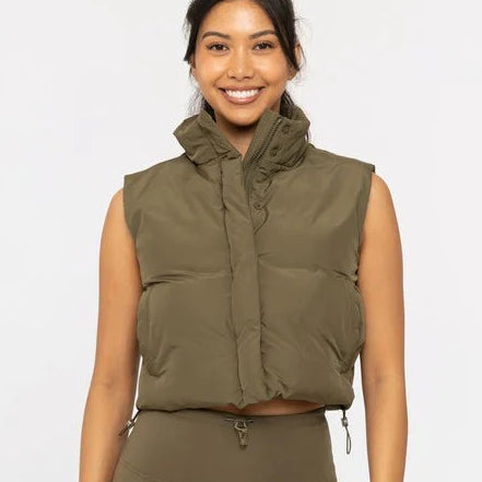 Woman wearing an olive green puffer vest and pants on a white background