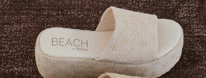 Four pairs of 'Beach' brand slippers in different patterns on a textured surface.