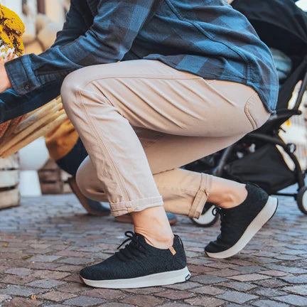 Person arranging yellow flowers in a wooden crate on a sidewalk.